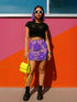 High waisted mini skirt with bold purple and pink floral print in a vibrant, maximalist style. Features a sculpted, body-hugging fit with a 1.5-inch elastic waistband that sits comfortably at the natural waist. Made from eco polyester and spandex blend that is stretchy, quick-drying, odor-resistant, and includes UPF 50 UV protection. Available in standard or glittery metallic finish in sizes S to XL.