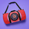 Red cylindrical duffle bag with black straps, featuring a prominent circular emblem with a colorful Baphomet design and "Hail Skatin" text. Includes mesh side pocket and adjustable padded shoulder strap.