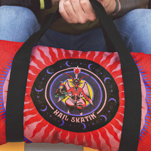 Red cylindrical roller skating duffle bag with black straps, featuring a prominent circular emblem with a colorful Baphomet design and "Hail Skatin" text. Includes mesh side pocket and adjustable padded shoulder strap.