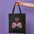 Canvas tote bag featuring pink skull cherries design. Two pink skulls connected by red stem and bow. Quirky gothic-inspired graphic on cream background. Stylish, edgy accessory for everyday use. Perfect for alternative fashion lovers.