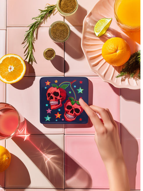 Square navy blue coasters featuring vibrant red cherry skulls with green stems and colorful star designs. Gothic drink coasters for maximalist home bar decor, whimsigoth table accessories perfect for weird decor enthusiasts and cocktail lovers.