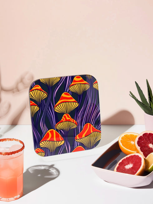 Square coasters featuring bright orange-red psychedelic mushrooms with yellow gills against deep purple background with flowing stems. Trippy magic mushroom drink coasters, funky retro barware, maximalist table decor, weird hippie home accessories.