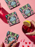 Square coasters featuring psychedelic blue cats with green eyes surrounded by baroque pink and green flourishes on black backgrounds. Gothic maximalist drink coasters for cat lovers, weird barware accessories, funky eclectic home decor, whimsigoth design.