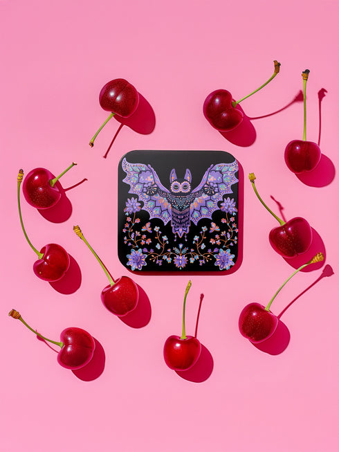 Square coasters featuring lavender-purple bats with folk art floral designs against black backgrounds. Pastel goth drink coasters, kawaii bat home decor, whimsigoth barware accessories, gothic floral table protection for weird home aesthetics.