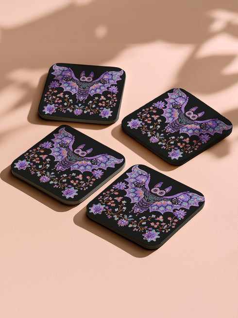 Square coasters featuring lavender-purple bats with folk art floral designs against black backgrounds. Pastel goth drink coasters, kawaii bat home decor, whimsigoth barware accessories, gothic floral table protection for weird home aesthetics.