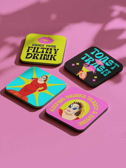 Four-piece coaster set featuring Divine/Pink Flamingos artwork with bold typography in pink, turquoise, and green. Includes "Toast to Trash," "Keeping Drinks Trashy," "Enjoy Your Filthy Drink," and Divine portrait designs.
