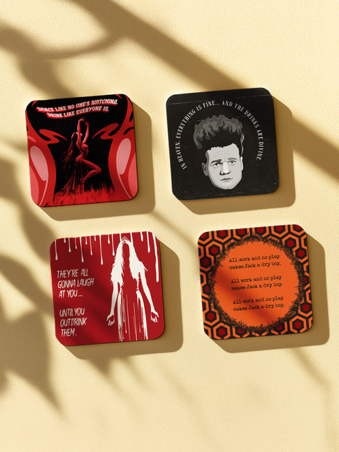 Four-piece horror movie coaster set featuring The Shining and Carrie designs in black, red, and orange with iconic quotes and imagery from the films. Cork-backed hardboard construction.