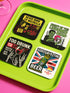 A set of four glossy square coasters on a vibrant green surface, each featuring a unique punk rock parody design. Top left: "Never Mind the Buzzkills" in yellow and pink ransom-note typography. Top right: "Night of the Liquored Dead" featuring a green zombie holding a drink in a horror comic style. Bottom left: "Too Drunk To Sip" with skeleton hands holding a wine glass on a black background. Bottom right: "God Save The Beer" featuring a green beer can on a Union Jack flag background.