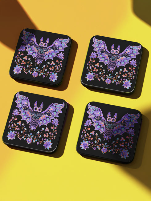 Square coasters featuring lavender-purple bats with folk art floral designs against black backgrounds. Pastel goth drink coasters, kawaii bat home decor, whimsigoth barware accessories, gothic floral table protection for weird home aesthetics.
