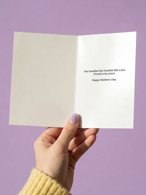 Funny Mother’s Day card in a 5x7 size featuring a vibrant chartreuse green background. The centralized design shows two pink hands with an electric blue eye in each palm, surrounded by cream stars. The retro bubble text reads "YOU RAISED A HANDFUL. PROUD OF YOU." A plum and pink geometric diamond border frames the card. This high-fidelity print mimics a 70s psychedelic art style with a flat matte or silk finish. A white sealable envelope is included with the handmade card.