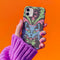 Phone case featuring baroque-style blue cat with green eyes surrounded by mint green foliage and pink flourishes on black background, Victorian-inspired desig