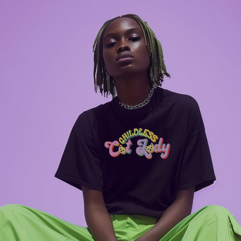 An election 2024 t-shirt with a colorful retro-style graphic that reads "Childless Cat Lady" across the chest. The text is in a playful, curvy font with each word in a different color - "Childless" in yellow-green, "Cat" in pink, and "Lady" in purple. Small cat face icons are incorporated into the letters 'a' in "Cat" and "Lady".