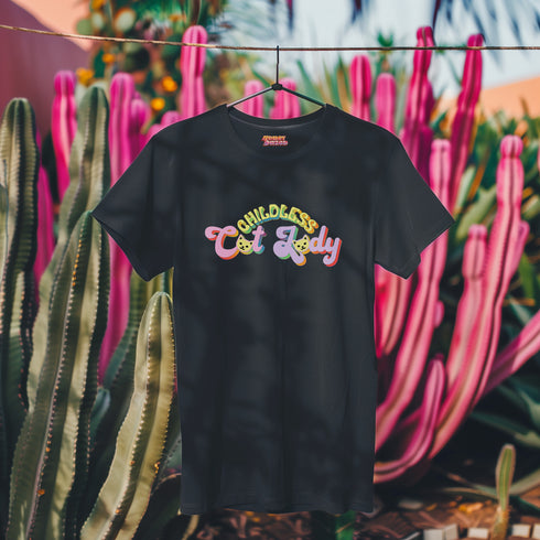 An election 2024 t-shirt with a colorful retro-style graphic that reads "Childless Cat Lady" across the chest. The text is in a playful, curvy font with each word in a different color - "Childless" in yellow-green, "Cat" in pink, and "Lady" in purple. Small cat face icons are incorporated into the letters 'a' in "Cat" and "Lady".