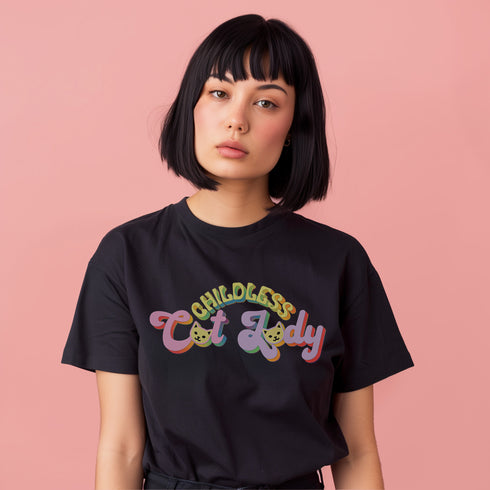 An election 2024 t-shirt with a colorful retro-style graphic that reads "Childless Cat Lady" across the chest. The text is in a playful, curvy font with each word in a different color - "Childless" in yellow-green, "Cat" in pink, and "Lady" in purple. Small cat face icons are incorporated into the letters 'a' in "Cat" and "Lady".