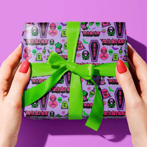Vibrant purple wrapping paper with gothic-inspired design for 50th birthdays. Features colorful skulls wearing party hats, coffins, 'RIP 40s' tombstones, and 'Youth Dies Here' text. Perfect for edgy, humorous gifts to 50-year-olds.
