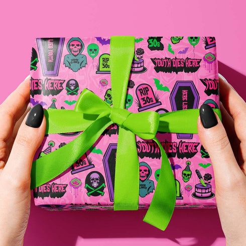 40th birthday Vibrant wrapping paper featuring a playful goth theme with illustrations of skulls, birthday cakes, and caskets marked "RIP 30s", set against a pink background with green accents. Ideal for themed 40th birthday gifts.