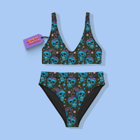 High-waisted bikini set featuring an all-over pattern of neon blue skulls with pink bows, pastel stars, and purple cherries on a dark olive green background. The top has a scoop neckline with wide straps, and the bottoms offer full coverage. A bold, punk-inspired swim look perfect for alternative fashion lovers and dopamine dressers.