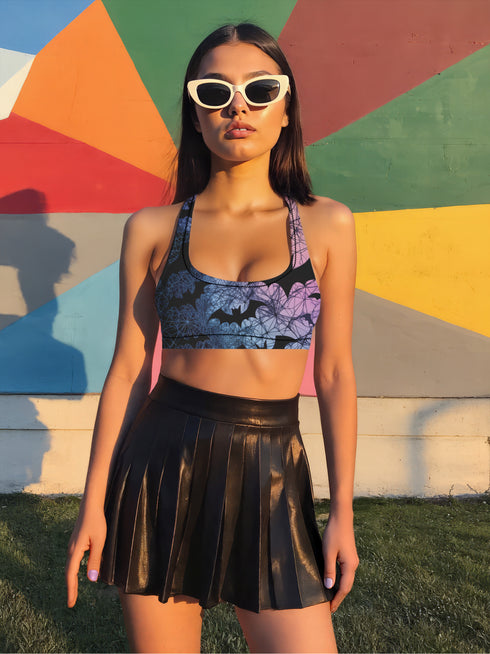 Model wearing a high-waisted pastel goth bikini set featuring a black bat and spiderweb print over an ombré pink and purple background. The two-piece swimsuit includes a scoop neck top and high-rise bottoms, styled outdoors in bright festival and poolside settings. Made of recycled fabric, soft, stretchy, and UV resistant. Available in XS to 3X. Aesthetic is gothic, spooky cute, and Y2K inspired.