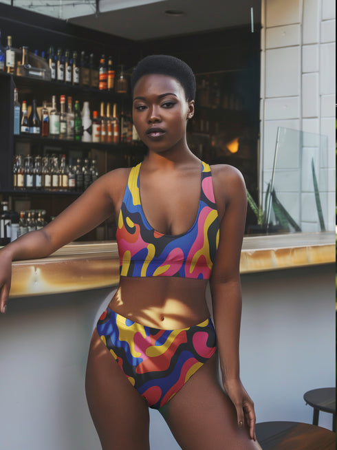 High-waisted bikini bottom with a vibrant wavy print in rainbow hues of pink, blue, yellow, orange, and navy on a black base. Features cheeky fit and double-layered fabric, styled over a bright turquoise pool for a sun-drenched summer look. Perfect for maximalist beachwear, retro pool parties, and colorful rave-inspired swim fashion.