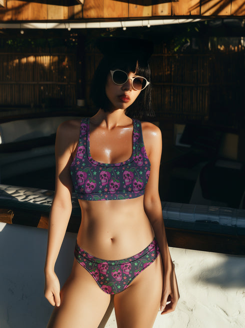 Two-piece bikini set featuring a bold pastel goth design with neon pink skulls wearing green bows, surrounded by multicolored stars on a deep black background. The set includes a plunging V-neck bikini top with wide straps and high-waisted bottoms for a flattering retro fit. Made of stretchy, soft material with a smooth black lining. This skull print swimsuit is ideal for alternative, edgy summer style with a playful punk twist.