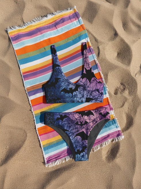 High-waisted bikini set with a gothic twist, featuring black bats flying across a dreamy gradient of pastel purple, pink, and blue spiderwebs. The top has a deep scoop neckline and thick straps, paired with full-coverage bottoms. Perfect for spooky sirens, pastel goths, and Halloween-loving hotties who haunt the beach year-round.