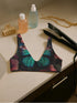 Scoop-neck bikini top with wide straps and a gothic butterfly wing design in deep jewel tones—teal, burgundy, and violet—set against black. Sports-bra style silhouette with bold symmetrical wing details across the chest. Floating above a turquoise pool, this swim top serves dreamy alt-girl energy for pool witches, celestial babes, and butterfly goths alike.