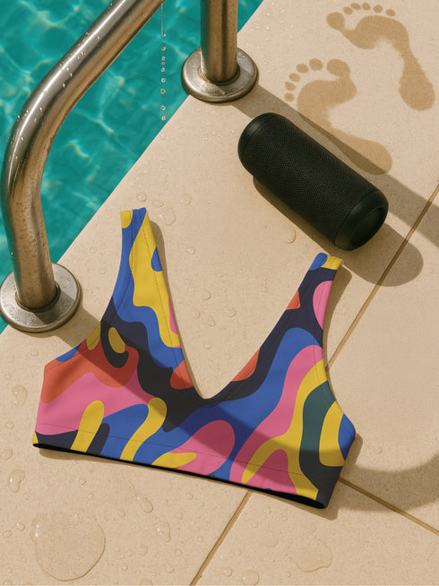 Scoop-neck bikini top with wide straps, featuring a bold psychedelic wave print in pink, yellow, blue, orange, and navy. Designed in a sports-bra style silhouette with supportive coverage and a vibrant Y2K vibe. Floating against a turquoise pool background, this top brings festival energy, dopamine brights, and funky retro flair to your swimwear drawer.