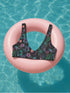 Black Cherry floral bikini top with deep V neckline, bold pink and purple tropical flowers, glossy leaves, and subtle fruit pattern. Made with recycled polyester and LYCRA, removable padding, double-layered, available in sizes XS to 3XL, features UPF 50 plus sun protection, non-reversible. Designed for festival, rave, and retro summer swim looks.