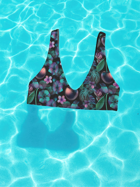 Black Cherry floral bikini top with deep V neckline, bold pink and purple tropical flowers, glossy leaves, and subtle fruit pattern. Made with recycled polyester and LYCRA, removable padding, double-layered, available in sizes XS to 3XL, features UPF 50 plus sun protection, non-reversible. Designed for festival, rave, and retro summer swim looks.