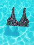 Black Cherry floral bikini top with deep V neckline, bold pink and purple tropical flowers, glossy leaves, and subtle fruit pattern. Made with recycled polyester and LYCRA, removable padding, double-layered, available in sizes XS to 3XL, features UPF 50 plus sun protection, non-reversible. Designed for festival, rave, and retro summer swim looks.
