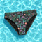 Dark Cherry floral bikini bottoms featuring a bold cherry and tropical flower pattern with deep green and purple leaves, made from moisture-wicking polyester and spandex, cheeky fit, mid-rise, available in sizes XS to 3XL, double-lined with UPF 50 plus sun protection. Perfect for rave outfits, summer festivals, beach goth, and retro pool parties.