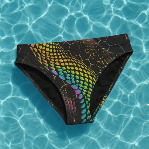High-waisted bikini bottom featuring a holographic snake scale print with neon rainbow tones on a sleek black background. Iridescent hexagon patterns add a futuristic edge. Cheeky fit with a double-layered finish, styled poolside against a bright turquoise water backdrop. Perfect for rave-ready swim looks, alternative beachwear, and bold festival swimwear with a Y2K cyberpunk twist.