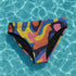 High-waisted bikini bottom with a vibrant wavy print in rainbow hues of pink, blue, yellow, orange, and navy on a black base. Features cheeky fit and double-layered fabric, styled over a bright turquoise pool for a sun-drenched summer look. Perfect for maximalist beachwear, retro pool parties, and colorful rave-inspired swim fashion.
