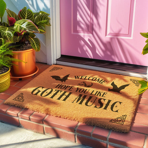 Tan coir doormat featuring "Welcome, Hope You Like Goth Music" in black text, with bat and skull imagery and gothic-style corner decorations.