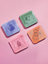 A set of four square coasters featuring humorous tarot card designs in pastel colors. The set includes a pink coaster titled 'High Priestess of Pour Decisions' showing a witch holding a goblet, a purple coaster titled 'Death of My Liver' depicting a skeleton holding a martini, an orange coaster titled 'The Lovers of Bad Idea Texts' featuring two hands toasting, and a green coaster titled 'The Hangover of Next-Day Regret' showing a skeleton falling. Glossy finish.