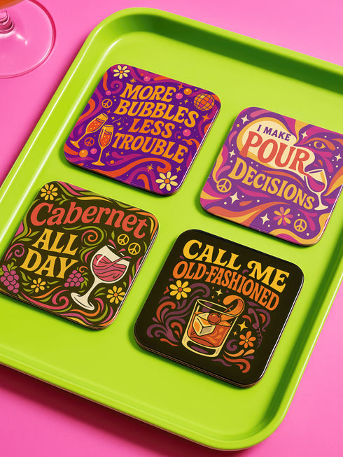 A 4-piece retro coaster set featuring colorful 70s-style cocktail graphics with playful drink quotes: "More Bubbles Less Trouble," "I Make Pour Decisions," "Cabernet All Day," and "Call Me Old-Fashioned." These 3.75” square coasters are made of Masonite with a glossy finish and cork backing—perfect for funky bar carts, dopamine décor, and retro hostess gifts.