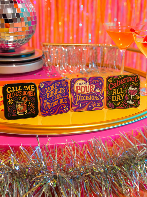 A 4-piece retro coaster set featuring colorful 70s-style cocktail graphics with playful drink quotes: "More Bubbles Less Trouble," "I Make Pour Decisions," "Cabernet All Day," and "Call Me Old-Fashioned." These 3.75” square coasters are made of Masonite with a glossy finish and cork backing—perfect for funky bar carts, dopamine décor, and retro hostess gifts.