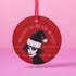 Round red metal Christmas ornament featuring Siouxsie Sioux in black and white with Santa hat, geometric patterns, and 'Spellbound by the Season' text, suspended by red ribbon