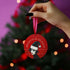 Round red metal Christmas ornament featuring Siouxsie Sioux in black and white with Santa hat, geometric patterns, and 'Spellbound by the Season' text, suspended by red ribbon