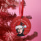 "Round red metal Christmas ornament featuring Nick Cave in black and white with Santa hat, Nordic patterns, and 'Where The Wild Mistletoes Grow' text, suspended by red ribbon