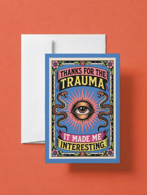 A 5x7 folded Mother's Day card with a vibrant cornflower blue background and traditional tattoo-inspired folk art. The front design is a centralized medallion featuring a realistic human eye at the center, surrounded by an orange and red radial sunburst. Two symmetrical tan and brown snakes frame the eye. Pink and yellow banners contain the black text "THANKS FOR THE TRAUMA IT MADE ME INTERESTING." Pink roses with green leaves are in corner.