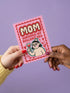 A 5x7 inch flat-printed pink greeting card featuring a cherry red scalloped border. At the top, bold wavy cream letters outlined in red read MOM. Below, red text says SURVIVED MY BULLSHIT ERA surrounded by small stars and hearts. The center illustration shows a smirking figure with black hair wearing small crown and holding a heart-shaped glass of \wine, outlined in light teal. The inside features black serif text: Bullshit era survivor award: you. Grateful you didn't quit on me. Love you, Mom.