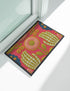 Pink outdoor doormat featuring a symmetrical folk art design. Two white skeleton hands with palms facing forward frame a large central pink and peach flower with a yellow center. Olive green stems, gold berries, and teal blue floral accents decorate the vibrant magenta background. The design mimics a textured embroidery look but is a flat 2d print. Framed with a sleek black border.