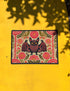 A rectangular beige doormat featuring a large, symmetrical folk art bat illustration in the center. The bat is black with coral red and mustard gold details that mimic the look of satin stitch embroidery. Surrounding the bat are stylized floral motifs in deep pink, coral, and olive green, arranged in a dense, decorative pattern. The texture visually resembles woven linen but is a smooth, flat print. The mat has a solid black trim border and is shown on a flat surface.