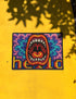 A rectangular indoor and outdoor doormat featuring a vibrant, psychedelic design. The central graphic is a large, open screaming red and orange mouth with white teeth, surrounded by highly saturated wavy, trippy patterns in blue, purple, magenta, and teal. Yellow stylized text reading HELLO is integrated into the pattern. The mat has a smooth 2D flat print surface that mimics the look of textured chainstitch embroidery, finished with a solid black fabric trim around all four outer edges.