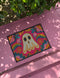 A rectangular polyester doormat with a vibrant, psychedelic design on a hot pink background. In the center is a cute, cartoonish ghost in off-white with yellow and orange outlines; it has large, dark, expressive eyes. The ghost is surrounded by a maximalist pattern of 70s-style floral motifs and puffy clouds in shades of teal, blue, orange, and light pink. Two small, colorful rainbows arc over the ghost's shoulders. The doormat has a durable, textured surface and is framed by a sleek black trim.