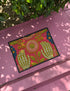 Pink outdoor doormat featuring a symmetrical folk art design. Two white skeleton hands with palms facing forward frame a large central pink and peach flower with a yellow center. Olive green stems, gold berries, and teal blue floral accents decorate the vibrant magenta background. The design mimics a textured embroidery look but is a flat 2d print. Framed with a sleek black border.