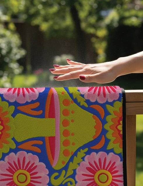 A rectangular polyester mat featuring a large central mushroom with a lime green cap, orange spots, and a pink underside. The design is surrounded by four large magenta and pink radial flowers with yellow centers. Bright green leaves and orange scrolling vines fill the spaces on a deep cobalt blue background. The artwork uses a tapestry-style visual effect to mimic the look of raised embroidery on a flat, printed surface. The mat is finished with a clean black stitched edge.