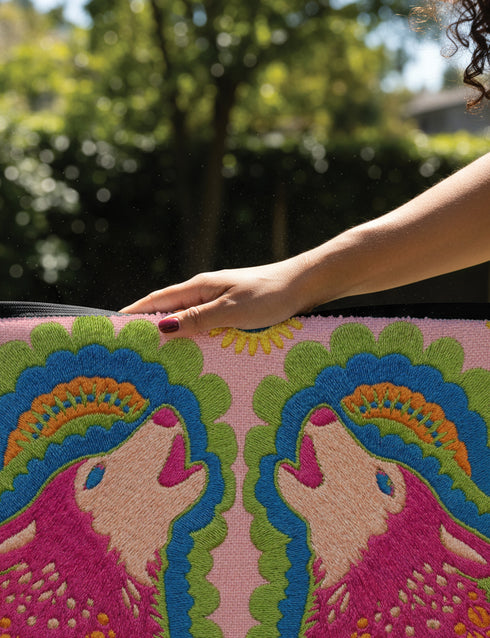 A rectangular outdoor doormat featuring a symmetrical graphic illustration of two howling wolves facing upward in profile. The design utilizes a vibrant psychedelic folk art style with a color palette of magenta pink wolves, peach muzzles, and scalloped layers of lime green and cyan blue foliage. A marigold yellow sun sits at the top center. The background is a dusty rose pink. The texture is a smooth, durable flat 2D print on polyester with a black non-slip rubber border.