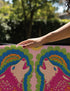 A rectangular outdoor doormat featuring a symmetrical graphic illustration of two howling wolves facing upward in profile. The design utilizes a vibrant psychedelic folk art style with a color palette of magenta pink wolves, peach muzzles, and scalloped layers of lime green and cyan blue foliage. A marigold yellow sun sits at the top center. The background is a dusty rose pink. The texture is a smooth, durable flat 2D print on polyester with a black non-slip rubber border.